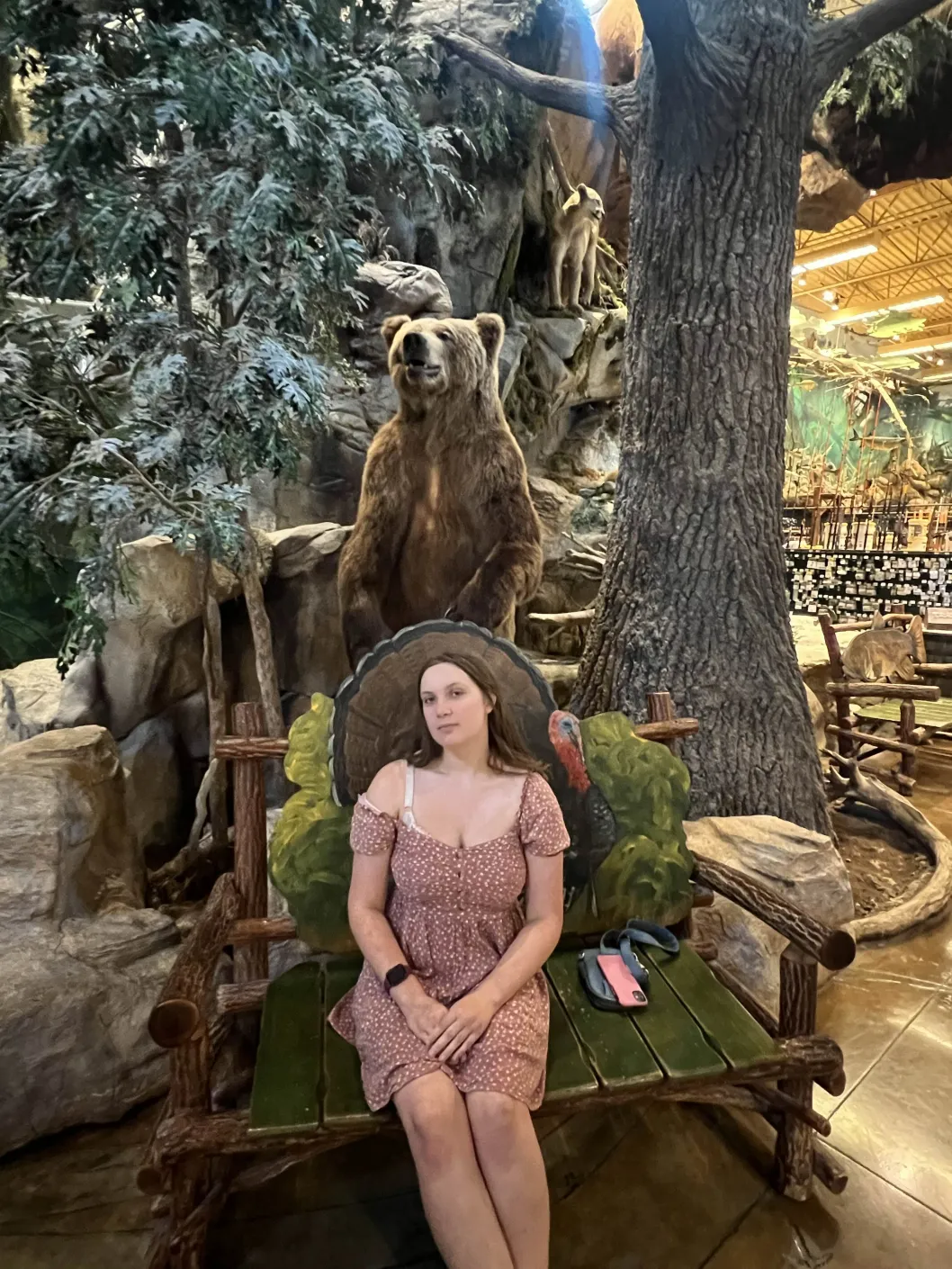 A young woman in a brown dress seated on a bench behind a bear in Bass Pro Shop
